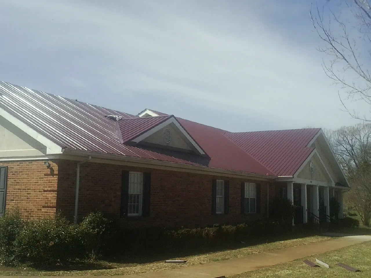 Red metal roof with gabled entries on a long brick building, from a Hail Damage Roof Repair job in Sutherland Springs