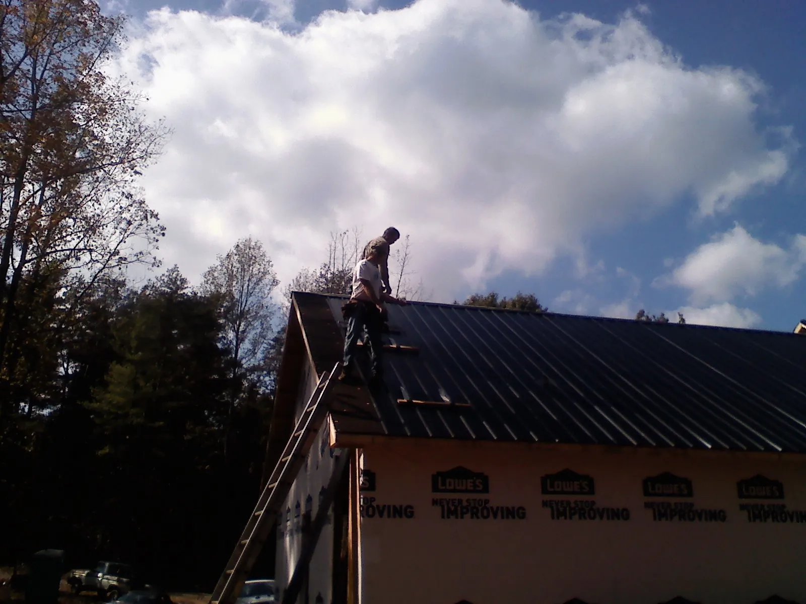 Roofer fastening dark metal panels high against a cloudy sky, from a Roof Inspection job in Sutherland Springs