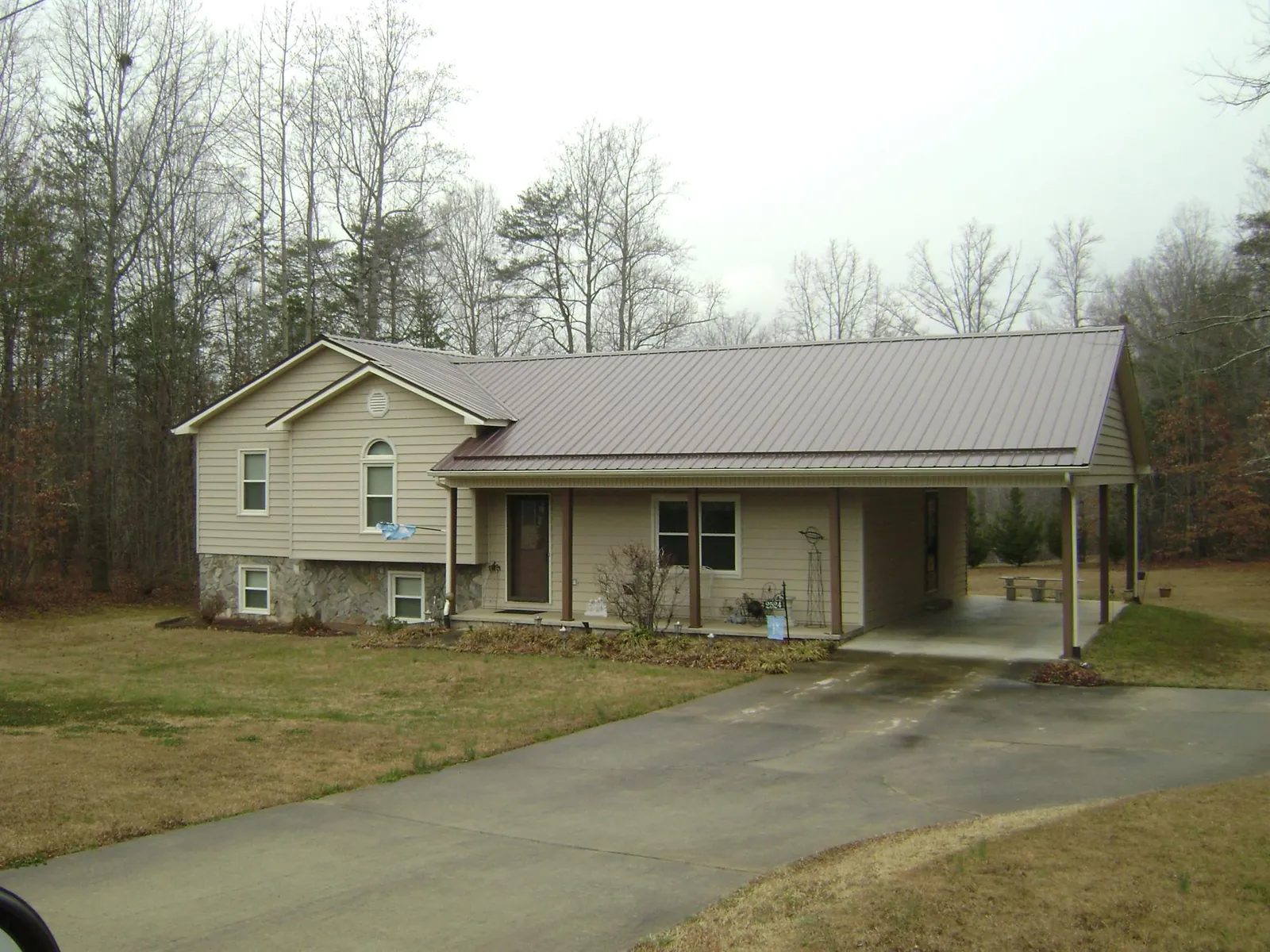 Brown metal roof on a tan split level home with an attached carport in Sutherland Springs