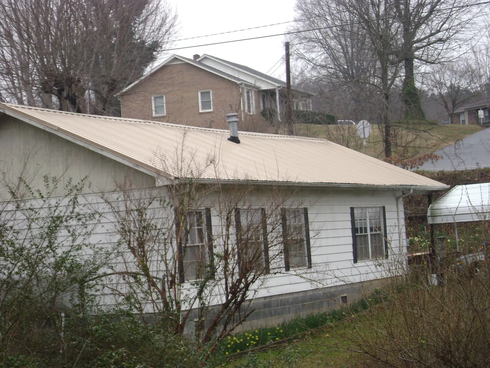 Tan metal roof on a white sided house set into a hillside — Commercial Roofing by Roofing Brothers in Sutherland Springs